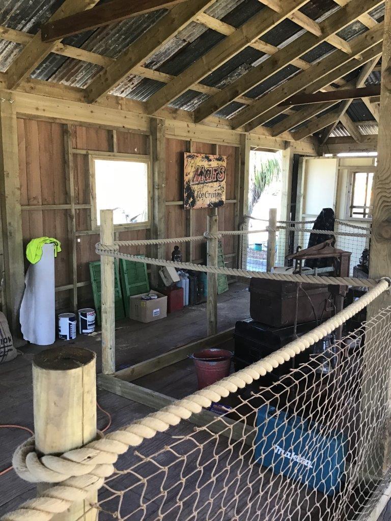Wooden interior of a structure with a rope barrier and various items on shelves.