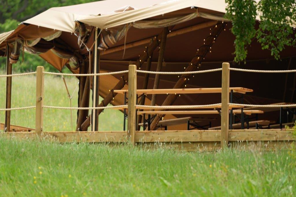 Tented accommodation with wooden deck and rope railings in a grassy outdoor setting