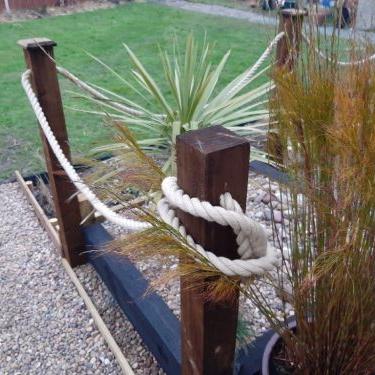 Decorative rope tied around wooden posts with plants in the background