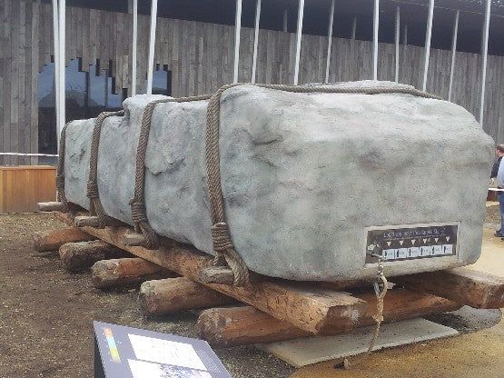 Large stone blocks secured with jute rope on wooden supports with a sign in front