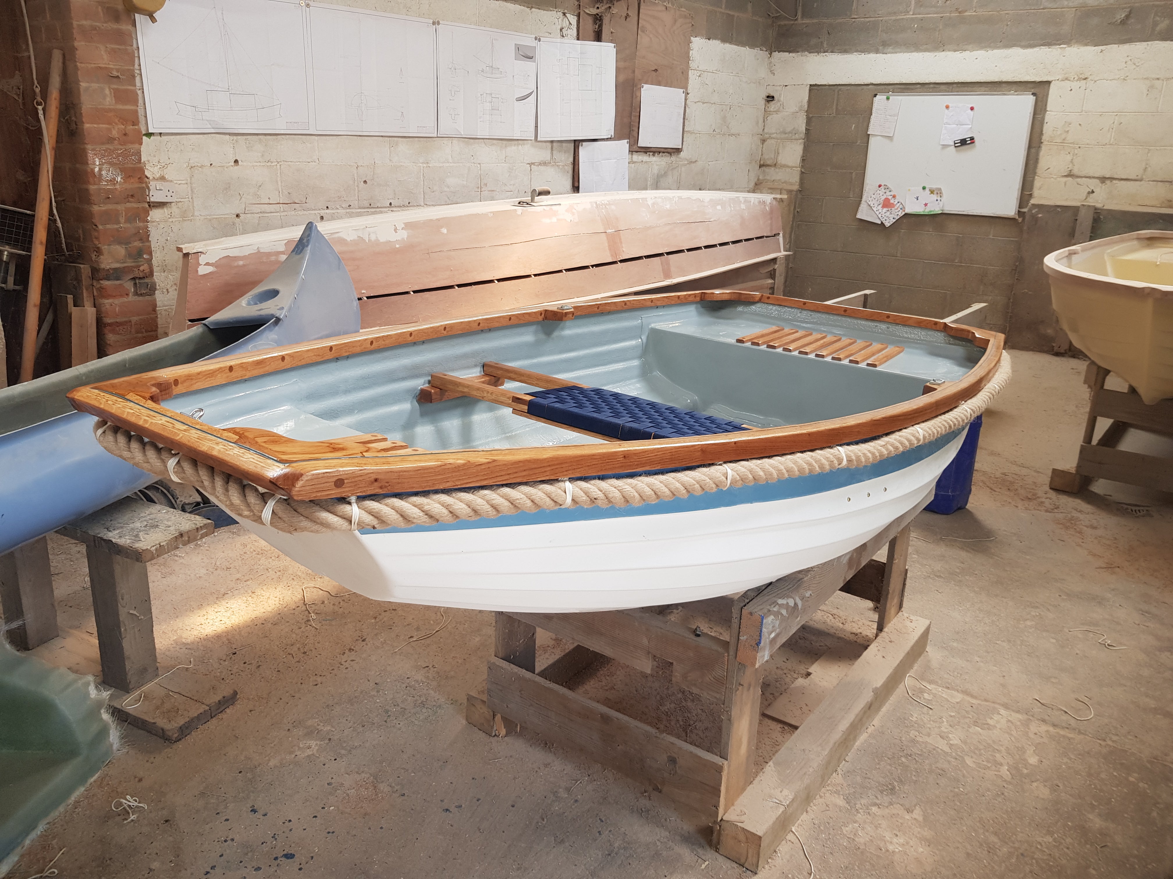 Small wooden boat with a 36mm jute rope fender on a stand in a workshop.